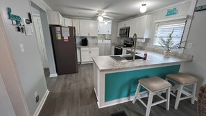 A modern kitchen with white cabinets, a central island with stools, a refrigerator, and a microwave. - SPACIOUS 4 BEDROOM/3 FULL BATH WITH GOLF CART! 3 MIN WALK TO THE BEACH! (Myrtle Beach)