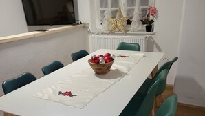A dining area with a white table, teal chairs, and a bowl of Christmas ornaments. - Pension Kostera, 1st Floor | 7 single beds & parking (Babenhausen)