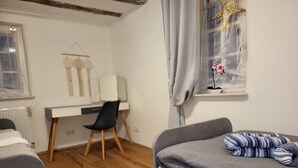 A bedroom with a bed, a desk, a chair, and a window with curtains. - Pension Kostera, 1st Floor | 7 single beds & parking (Babenhausen)