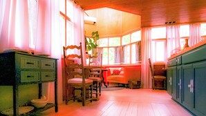 Une pièce avec un plancher en bois, une chaise en bois, une table avec de la vaisselle et un buffet.