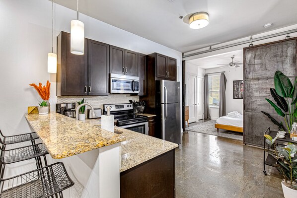 A modern kitchen with dark cabinets, stainless steel appliances, and a granite countertop. - Lofts On 30Th Ave (Nashville)