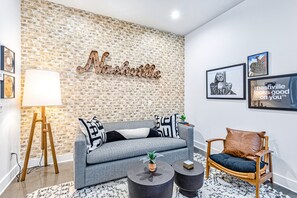 Una sala de estar moderna con una pared de ladrillo, un sofá gris, una silla de madera y una mesa de centro.
