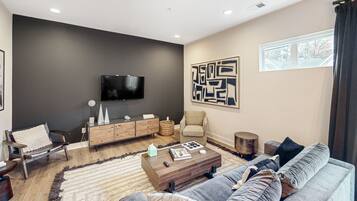 A modern living room with a flat-screen TV mounted on the wall, a sofa, a coffee table, and a large abstract artwork.
