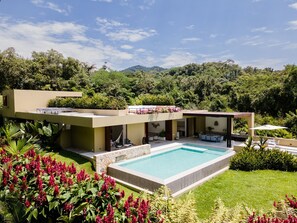 A modern house with a swimming pool, outdoor seating, and lush greenery.