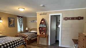 A room with two beds, a wooden dresser, a small table, and a wall-mounted shelf with decorative items.