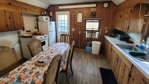 Eine kompakte Küche mit Holzausstattung, einem Esstisch mit Blumenmuster auf der Tischdecke, einem Kühlschrank, einem Herd und einer Mikrowelle.