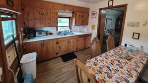 Eine kompakte Küche mit Holzschränken, einem Waschbecken und einem Essbereich mit einem Tisch, der mit einer gemusterten Tischdecke bedeckt ist.