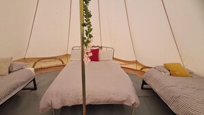 Ein Zelt mit drei Betten, jedes mit gestreifter Bettwäsche und Kissen in verschiedenen Farben.
