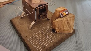 Ein Zelt mit Holzofen, Metallgestell und einer Snackbox auf einem Baumstumpf.