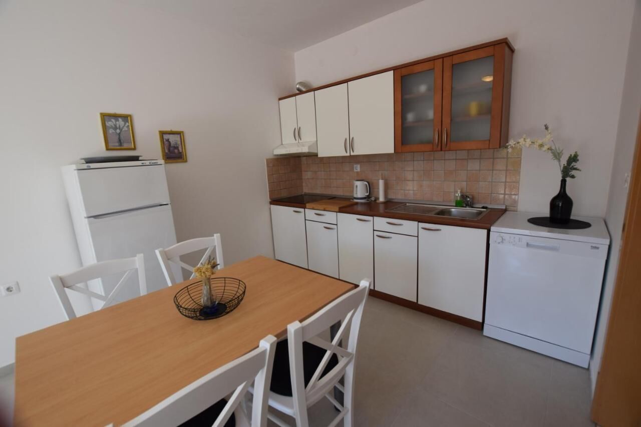 Een kleine keuken met witte kasten, een houten aanrecht, een witte koelkast, een vaatwasser en een eettafel met stoelen.