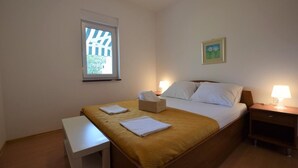 Habitación de hotel con cama, mesitas de noche, un pequeño escritorio, ventana con vistas y un cuadro en la pared.