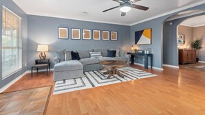 Un salon avec un canapé gris, une table basse ronde et un ventilateur de plafond.