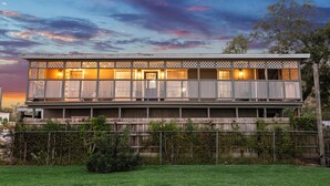 Un bâtiment à deux étages doté d’un balcon, d’une clôture en bois et d’une cour gazonnée.