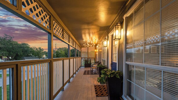 Une véranda couverte avec une balustrade en bois, des plantes en pot et une vue sur le coucher du soleil.