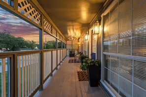A covered porch with a wooden railing, potted plants, and a view of the sunset.
