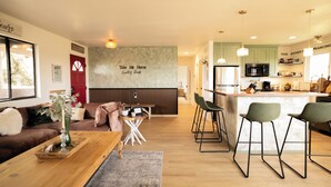 A modern living room with a wooden coffee table, a sofa, and a dining area with bar stools. A kitchen with a microwave and a sink is visible in the background. - Country Living on 1 acre in Paso Robles w/ AC, BBQ, starry nights, Dogs welcome (Paso Robles)