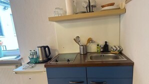 Cocina compacta con un lavamanos, hervidor de agua y cafetera. Hay armarios y una ventana con vistas al exterior.