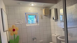 Un baño con inodoro, lavamanos, ventana y una decoración floral sobre un soporte de madera.