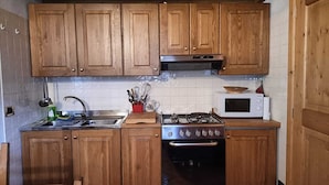 Una cocina con armarios de madera, estufa a gas, microondas y pileta.