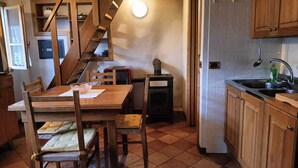 Una cocina con gabinetes de madera, piso de baldosas, una mesa de comedor de madera con sillas, estufa empotrada y una escalera que sube a un nivel superior.
