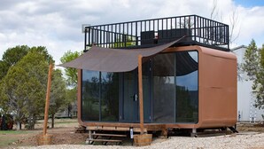 Une cabine moderne et compacte, dotée d’une grande porte coulissante, d’un balcon avec une rambarde en métal et d’une petite table en bois à l’extérieur.