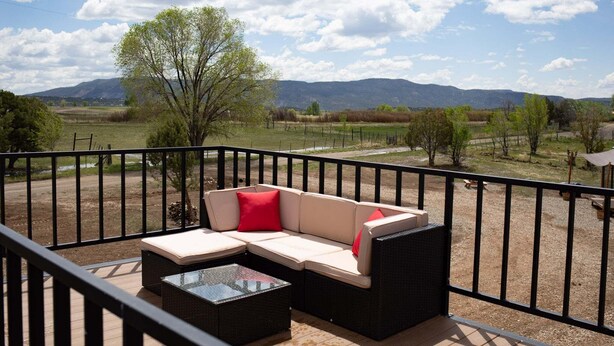 Un balcon avec un canapé et une table en verre, donnant sur un paysage rural avec des montagnes et des arbres.