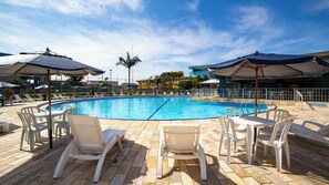 A swimming pool with lounge chairs and umbrellas, surrounded by a tiled deck and a fence.
