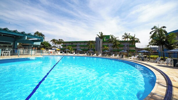 Una gran piscina al aire libre con sillas de descanso y sombrillas, rodeada de palmeras y un edificio de hotel.