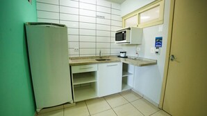 Una cocina compacta con alacenas blancas, un microondas integrado, un lavamanos y un refrigerador.