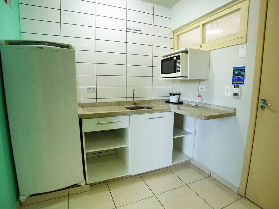 A compact kitchen with white cabinets, a built-in microwave, a sink, and a refrigerator.