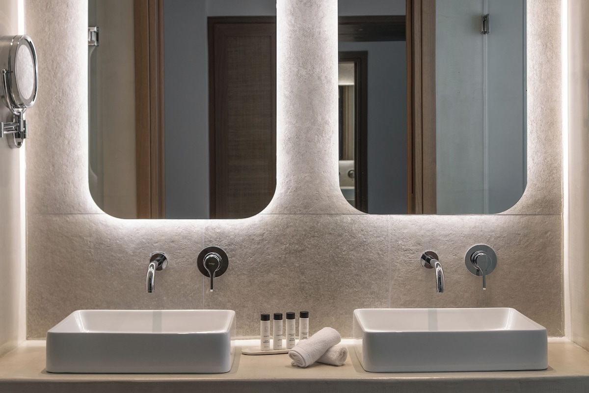 A bathroom with two sinks, each with a mirror above. There are towels and toiletries on the counter.
