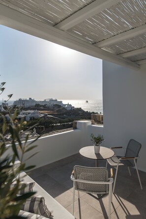 A balcony with a view of the sea, a round table, two wicker chairs, and a potted plant. - Arocaria Hotel (Mykonos)