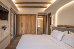 A modern bedroom with a large bed, wooden wardrobe, and a potted plant. - Arocaria Hotel (Mykonos)