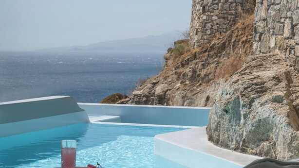 Un espace aménagé au bord de la piscine, avec un mur en pierre, une table sur laquelle est posée une boisson et un fauteuil en forme de sac de haricots.