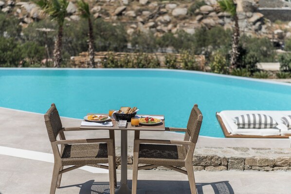 A dining table with wicker chairs and a view of a pool. - Arocaria Hotel (Mykonos)
