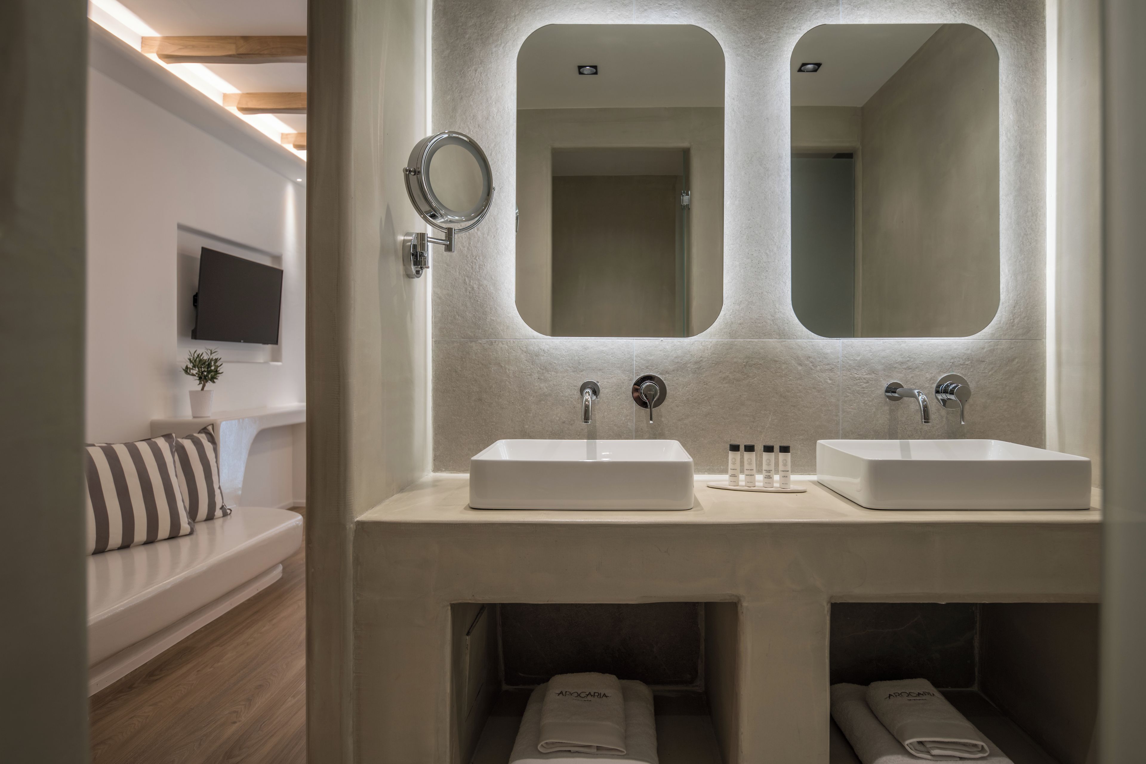 A modern bathroom with two sinks, a large mirror, and a built-in bench with towels.
