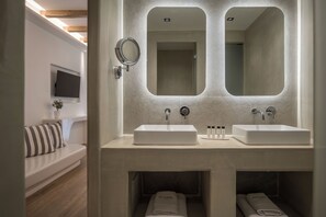 A modern bathroom with two sinks, a large mirror, and a built-in bench with towels. - Arocaria Hotel (Mykonos)