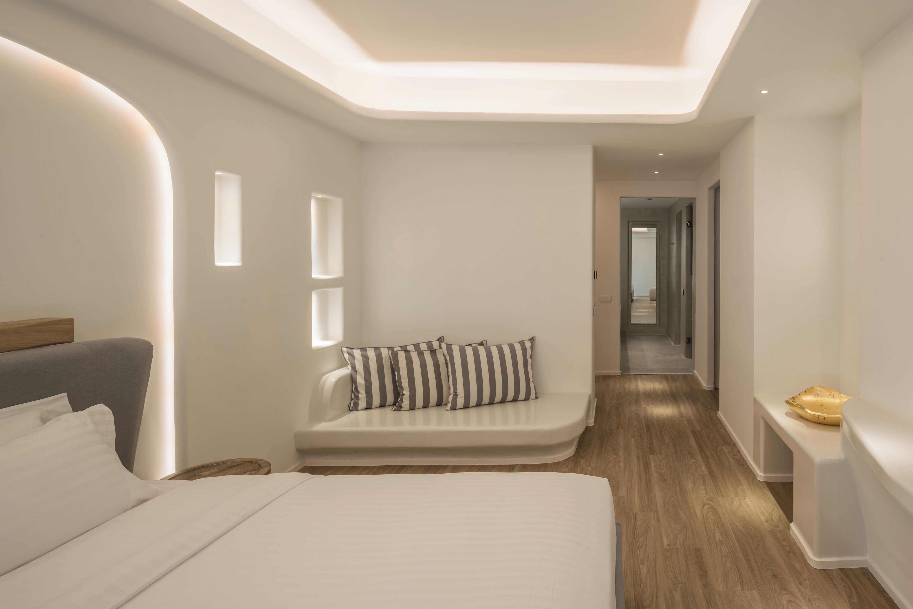 Quarto de hotel moderno com uma cama grande, um espaço de estar com almofadas listradas e piso de madeira.
