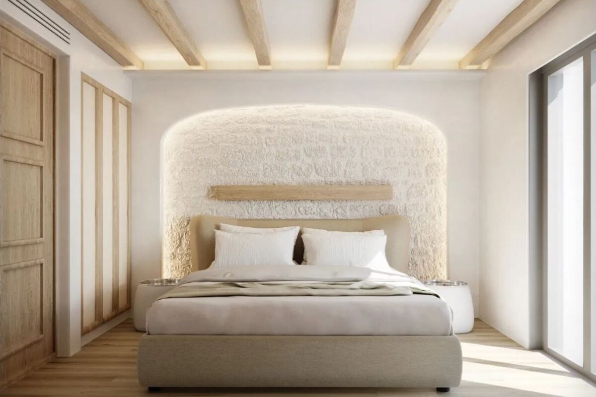 A modern bedroom with a large bed, a textured wall behind the bed, wooden beams on the ceiling, and a large window on the right.