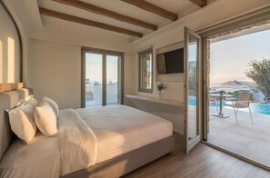 A bedroom with a large bed, a TV mounted on the wall, and a sliding glass door leading to a balcony with a pool. - Arocaria Hotel (Mykonos)