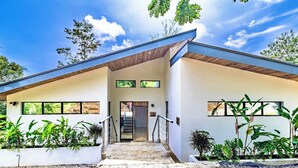 A modern two-story house with a flat roof, large windows, and a staircase leading to the entrance. - Private Eco-Luxury Villa near Rio Celeste | Jacuzzi • Nature • Sleeps 8 • (El Higueron de Upala)