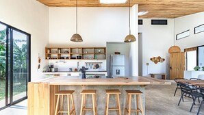 A modern kitchen with a large island, wooden stools, and pendant lighting. - Private Eco-Luxury Villa near Rio Celeste | Jacuzzi • Nature • Sleeps 8 • (El Higueron de Upala)