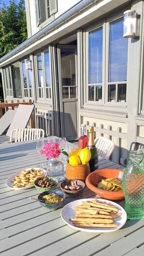 An outdoor dining table with various food items, a bottle of champagne, and a decorative vase.