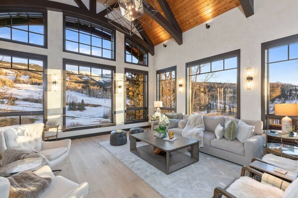 A spacious living room with large windows offering a view of a snowy landscape, a comfortable sofa, and a coffee table. - Vista Haus at Country Club - golf and ski retreat! (Mountain Village)