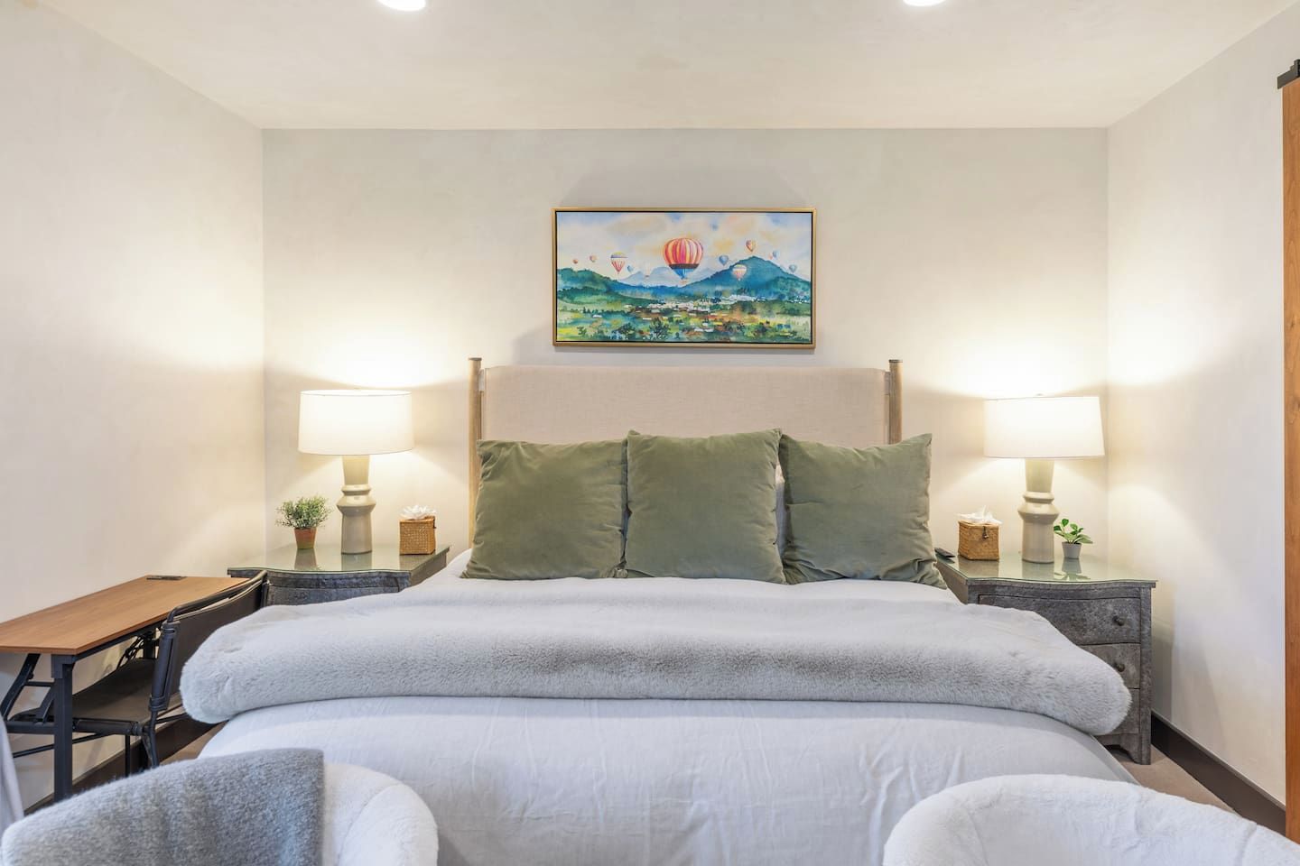Une chambre d’hôtel avec un lit, deux tables de chevet avec des lampes, un tableau au mur et une petite table avec une plante.