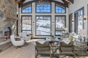 A spacious living area with a stone fireplace, large windows offering a view of a snowy landscape, and modern furniture.