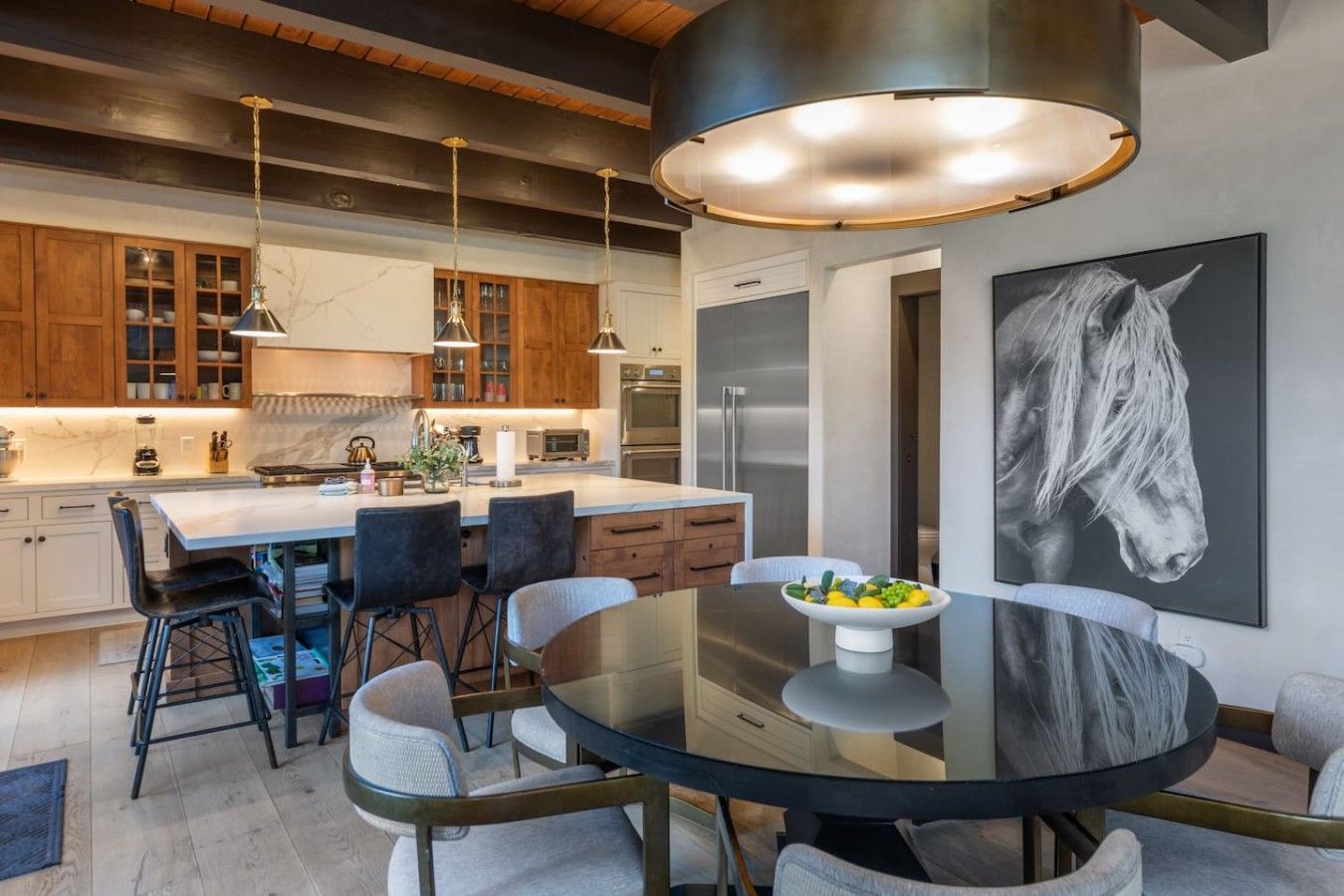 A modern kitchen with wooden cabinets, a central island, and a dining area with a glass table and chairs.