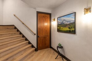 A wooden staircase leading to a door, a framed landscape painting, and a small table with a plant.
