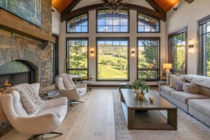 A spacious living room with a stone fireplace, large windows offering a view of a golf course, and modern furniture. - Vista Haus at Country Club - golf and ski retreat! (Mountain Village)
