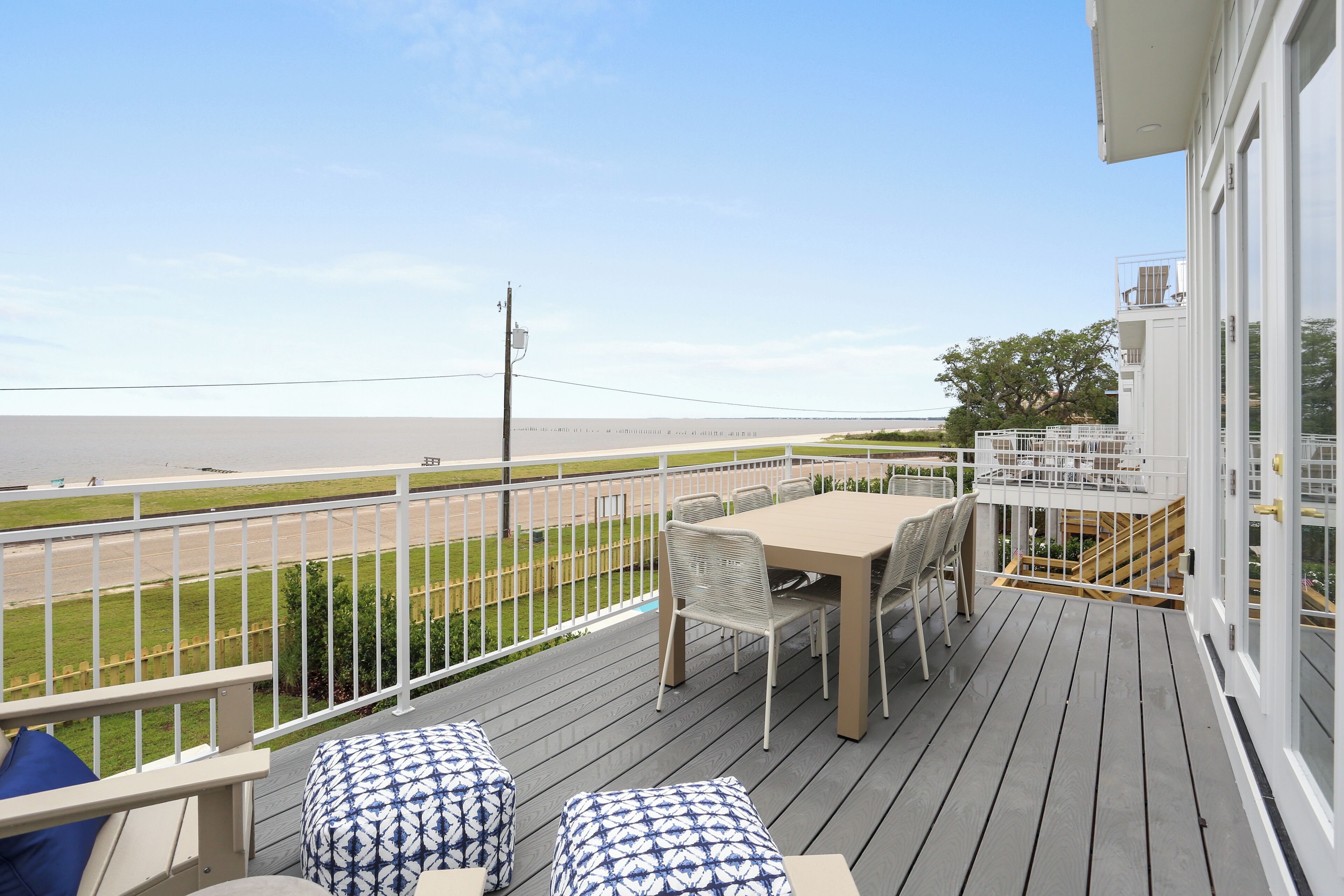 A deck with a table and chairs, overlooking a beach and a road.